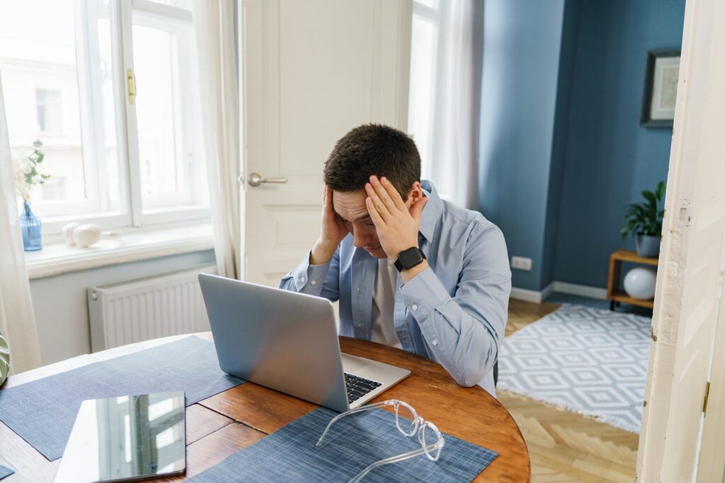 A stressed man in business casual attire grapples with a challenge on his laptop